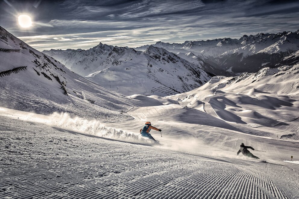 Perfectly groomed ski slope with two athletic skiers in Silvretta Montafon – the largest and most dynamic ski area in the Montafon Brandnertal region of the Austrian Alps.